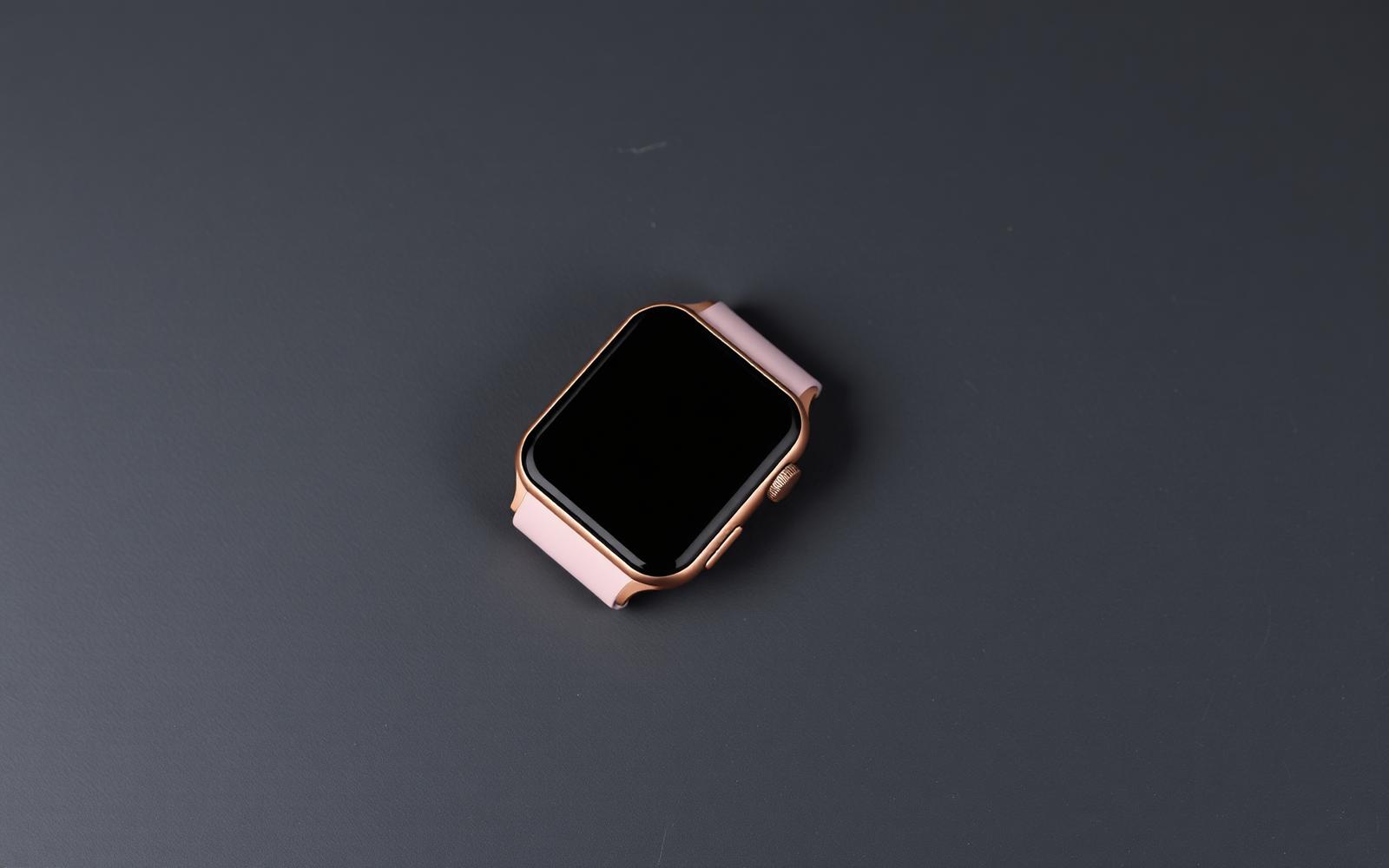 Vierkante smartwatch met rosegouden kast en lichtroze sportbandje op een donkere leisteen ondergrond